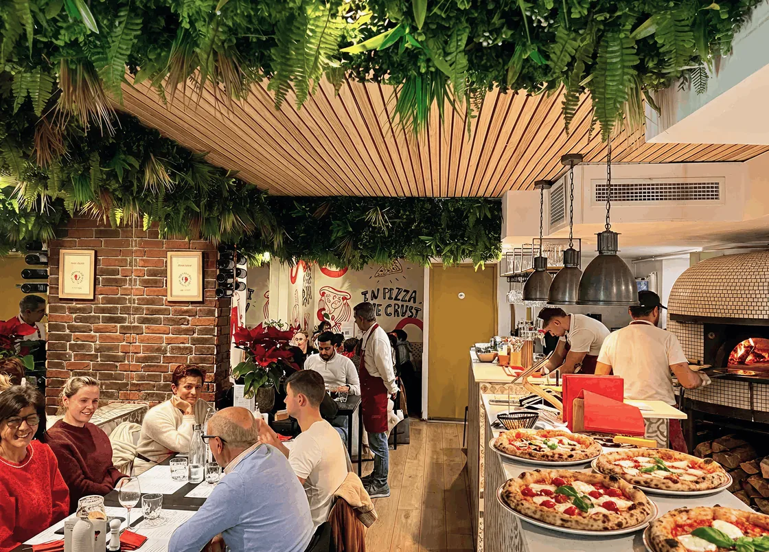 The Californie dining room under its ceiling of plants, pizzas lined up on the counter