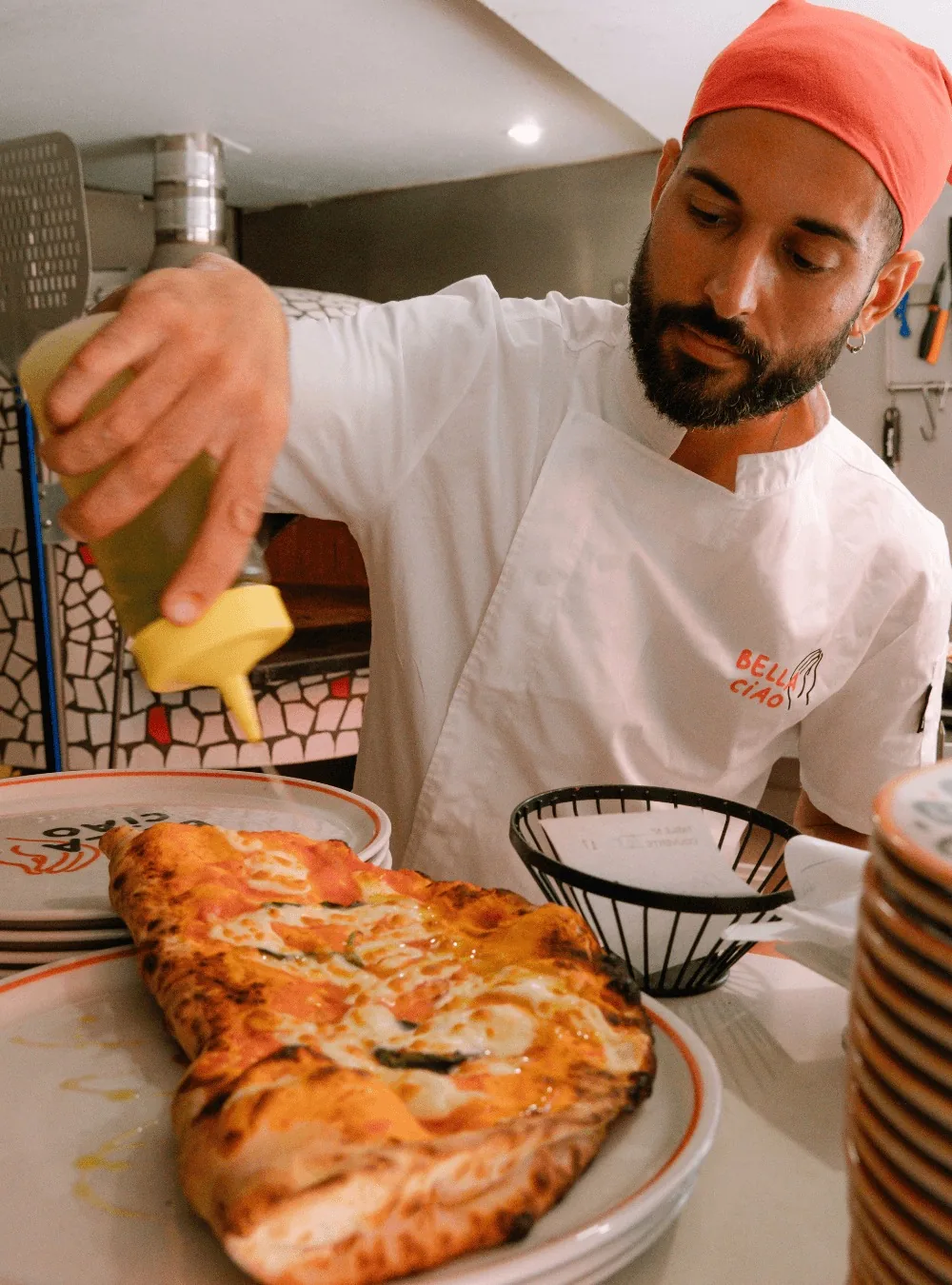 A pizzaiolo in his Bella Ciao chef jacket finishing a folded pizza with olive oil